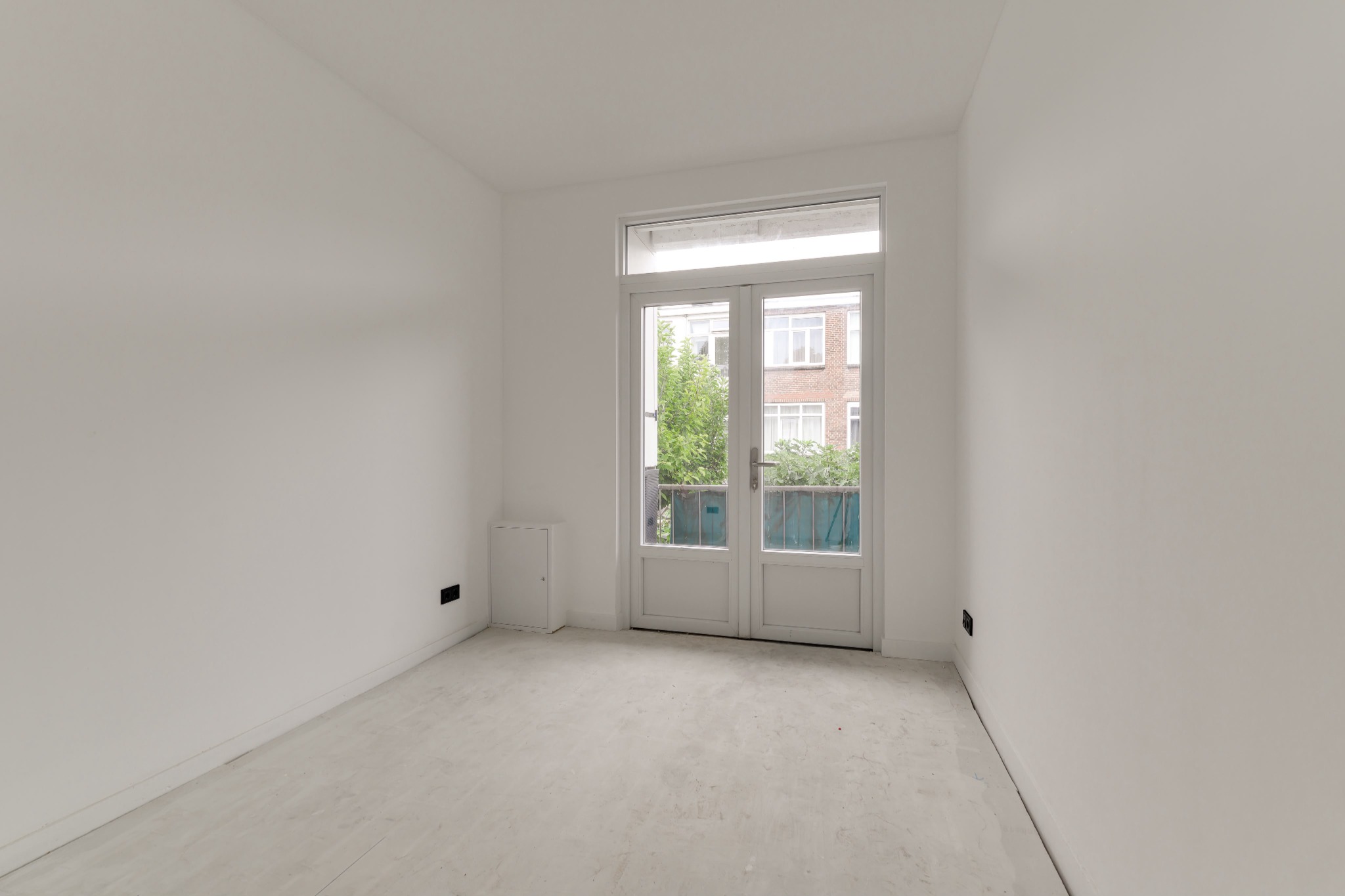 Lege, afgewerkte kamer met lichte wanden en openslaande deuren naar buiten.
