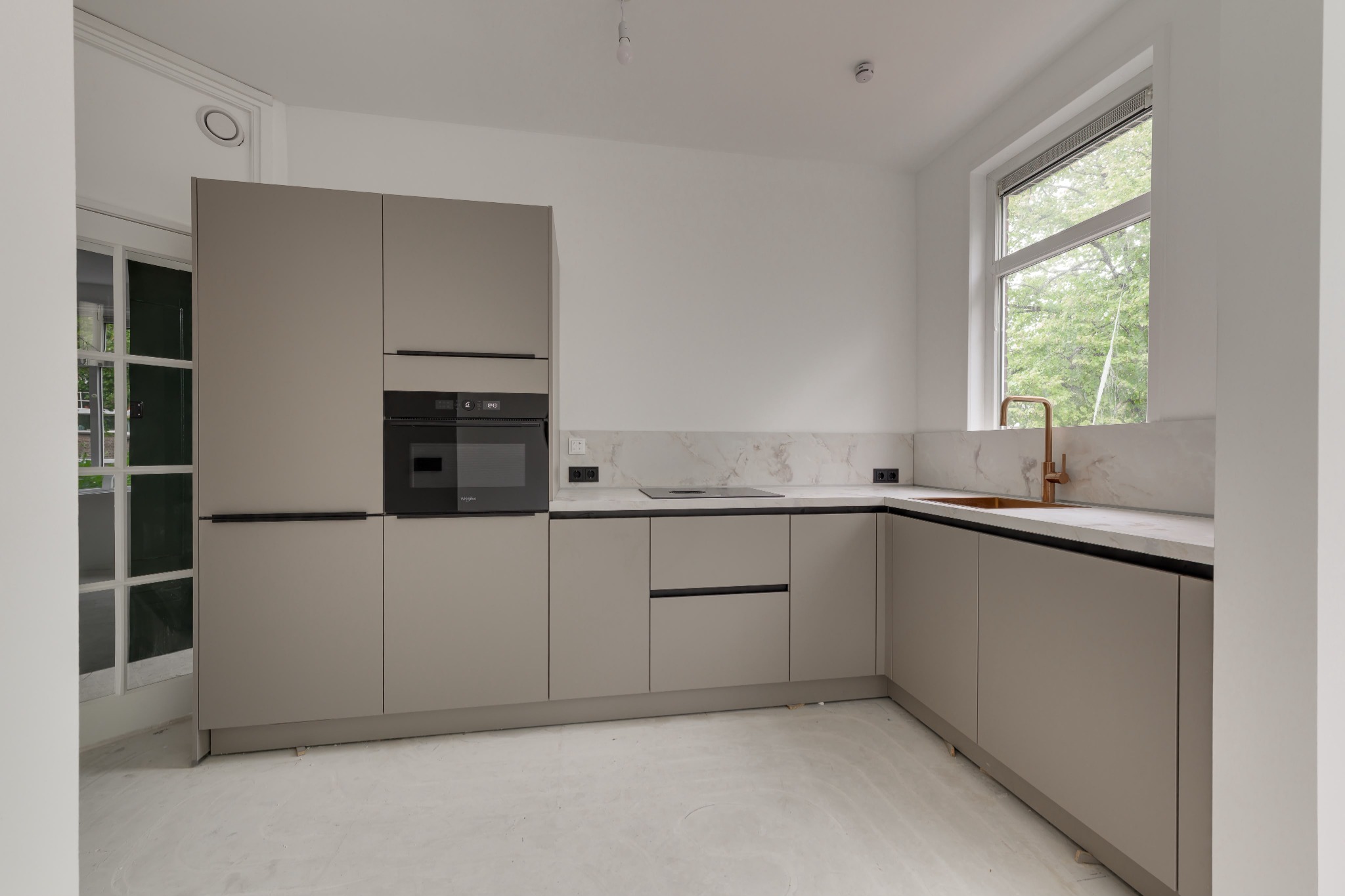 De lichte hoekkeuken vóór het inrichten van de ruimte, met beige keukenkasten en afgewerkte wanden.
