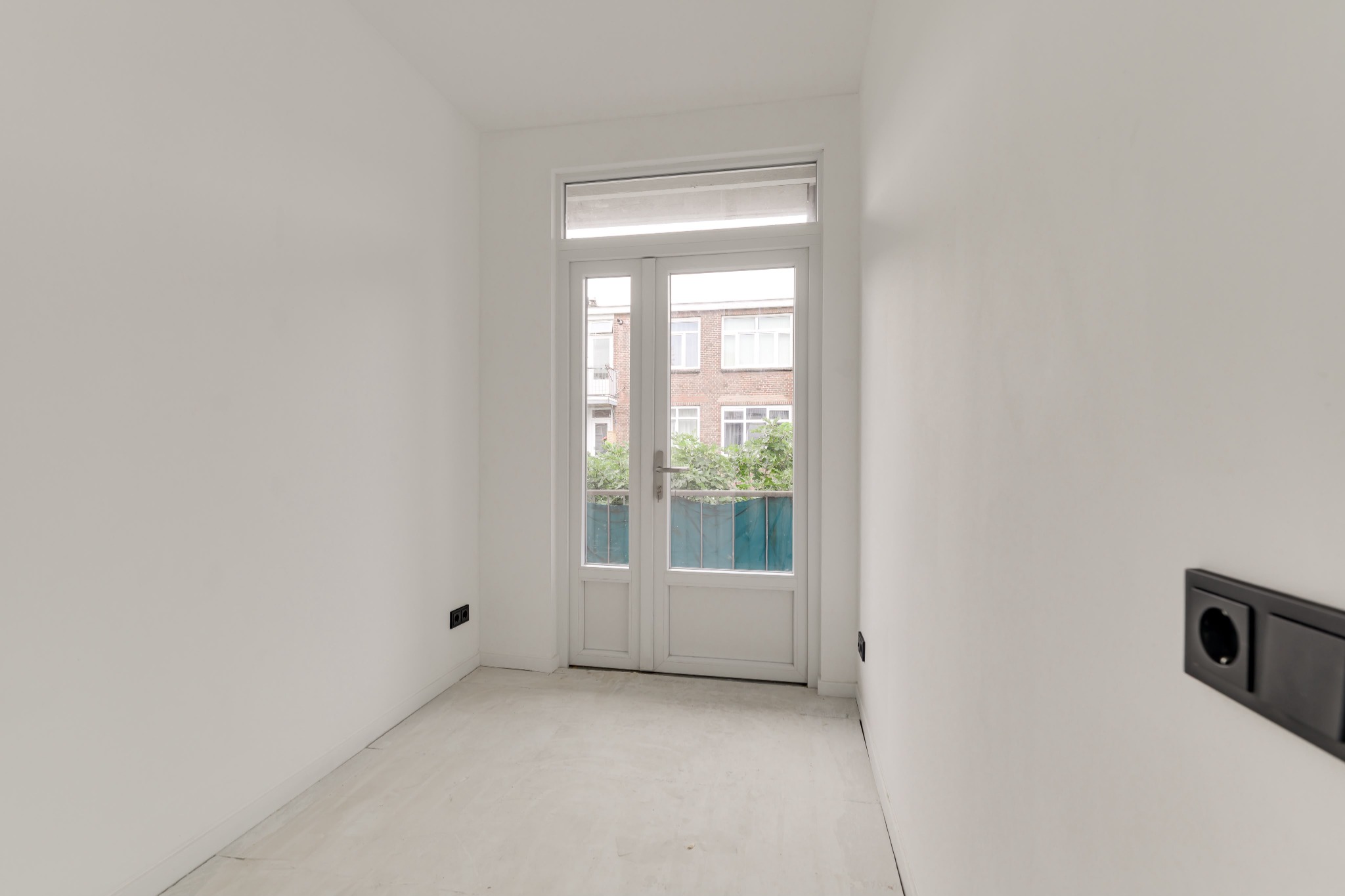 Lege, afgewerkte slaapkamer met lichte wanden en openslaande deuren naar buiten.