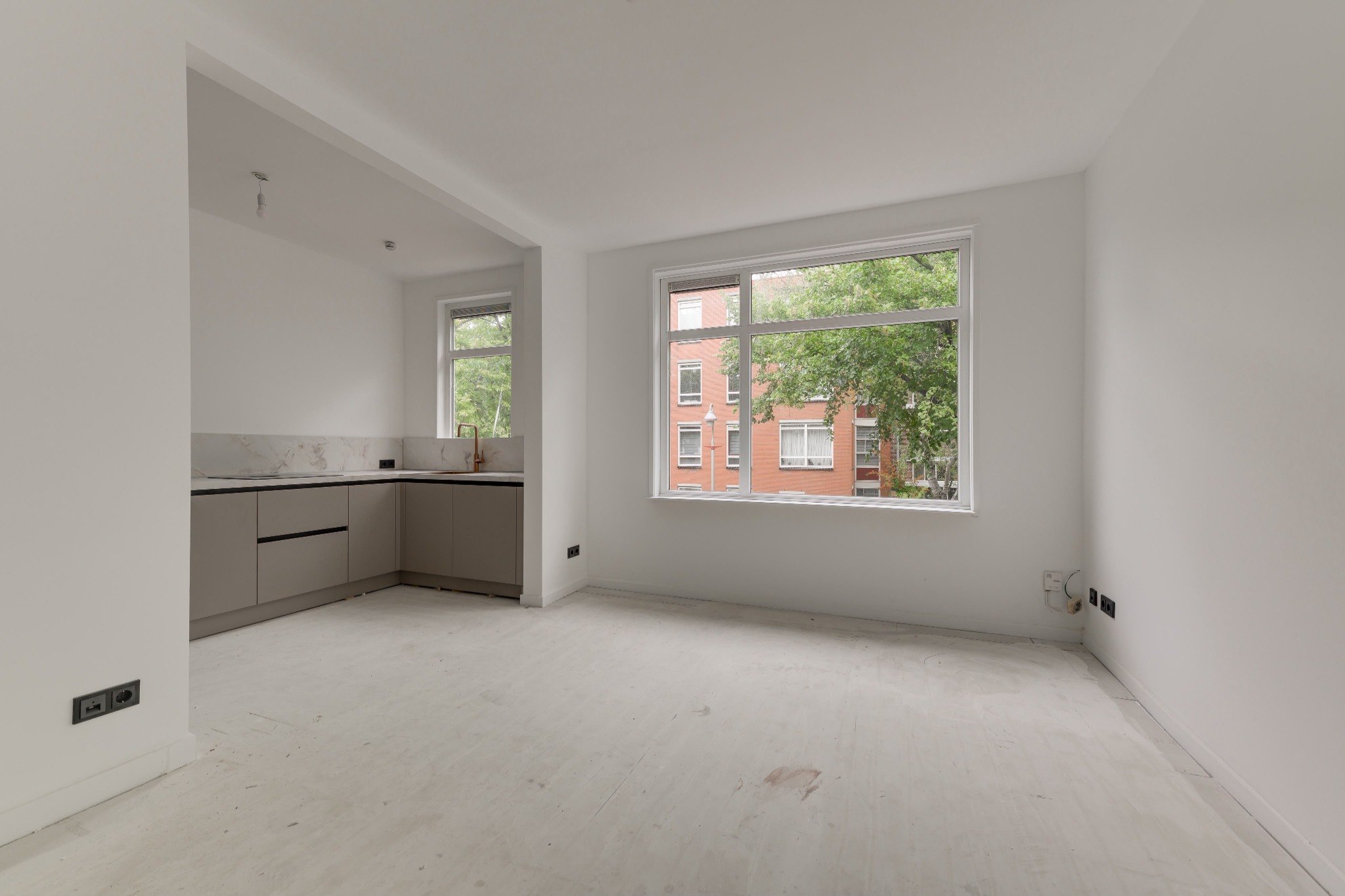 Breed beeld van de lege woonkamer na renovatie, met lichte wanden en zicht op de aangrenzende keuken.